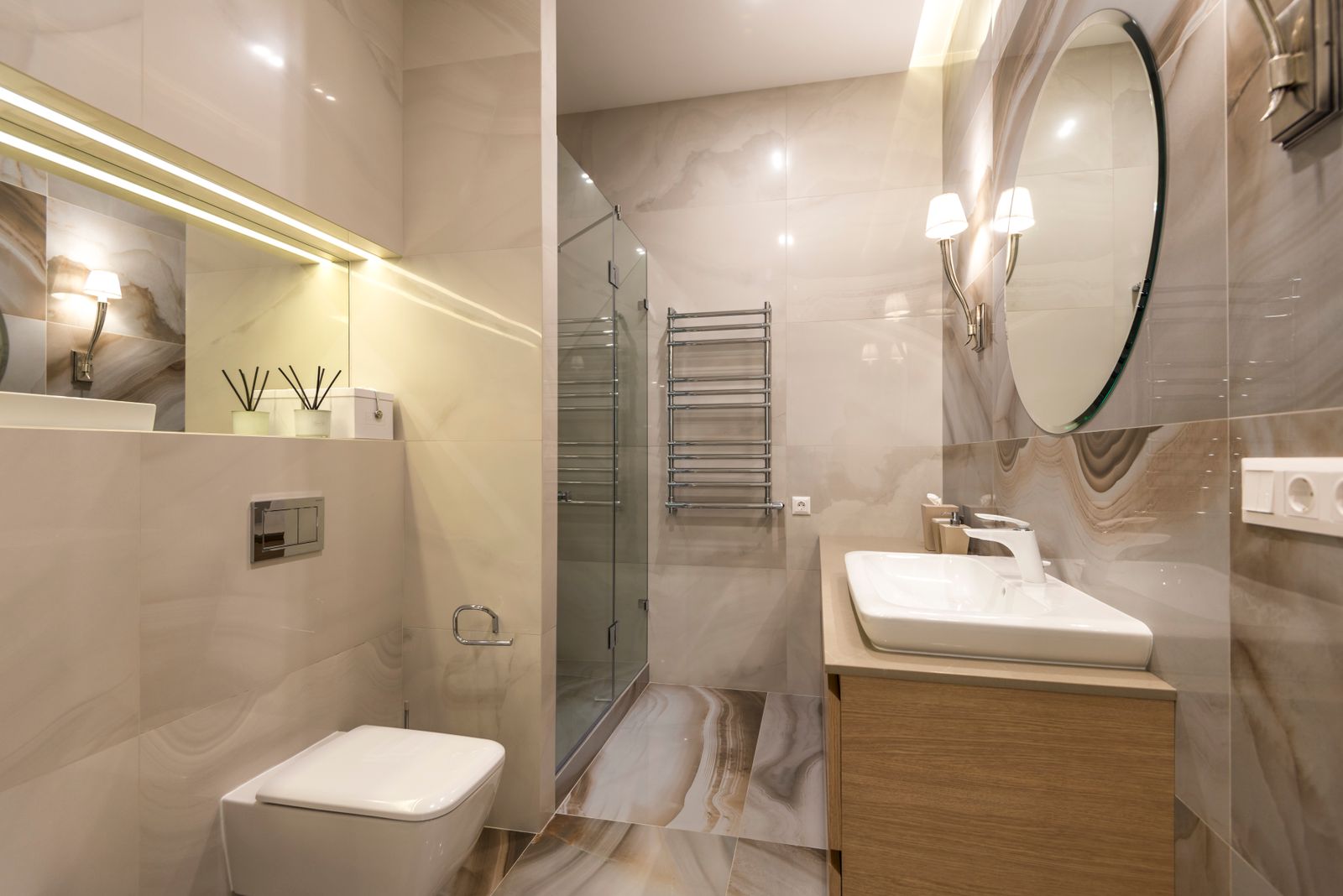 Petite salle de bain moderne aux tons beige et bois, avec meuble vasque suspendu, WC suspendu et grand miroir rond