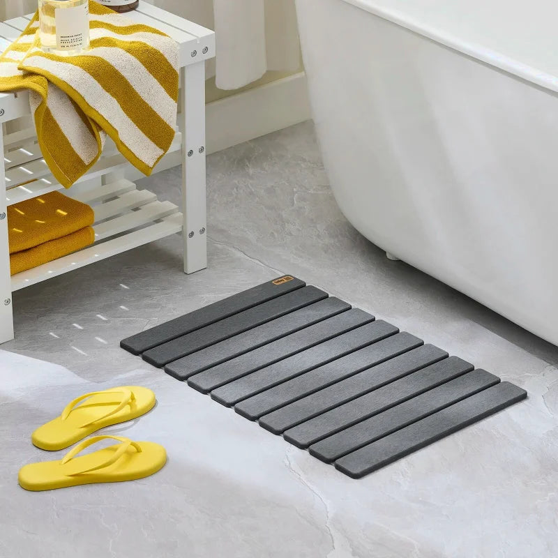 Tapis de bain gris placé sur le sol d’une salle de bain près d’une baignoire avec des sandales jaunes.