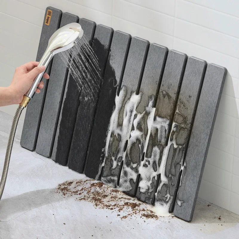 Tapis de bain gris rincé à l’eau pour montrer la facilité de nettoyage et l’évacuation des saletés.