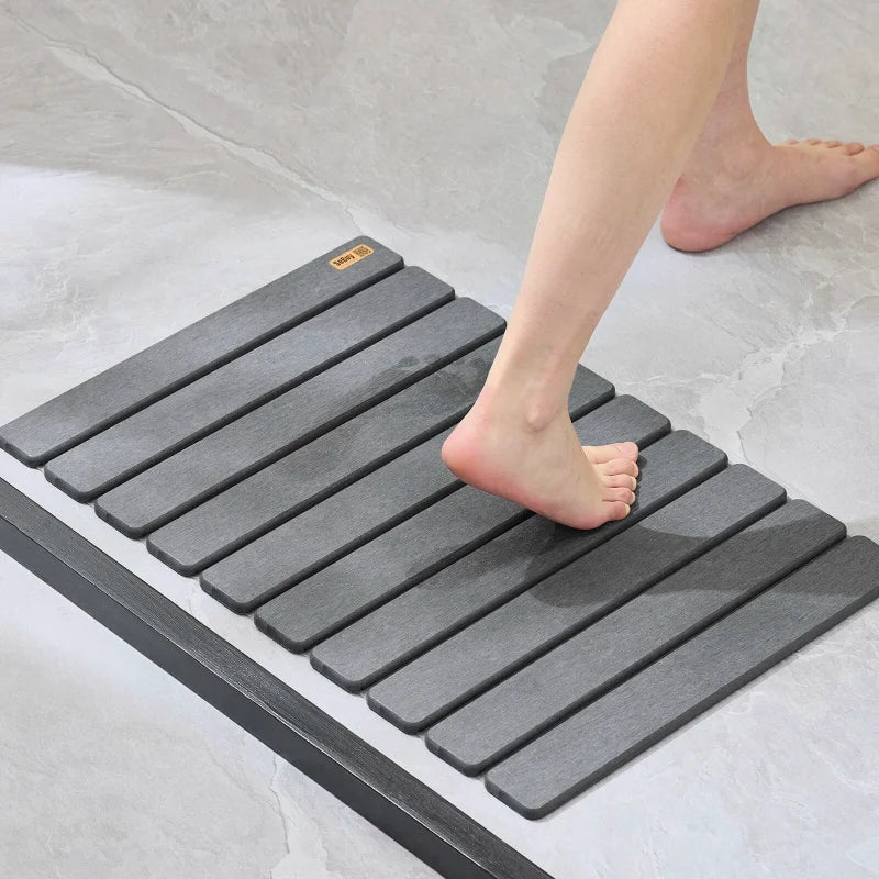 Pied nu marchant sur un tapis de bain gris antidérapant à lattes.