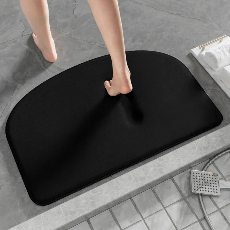 Pied nu marchant sur un tapis de bain gris à mémoire de forme noir.