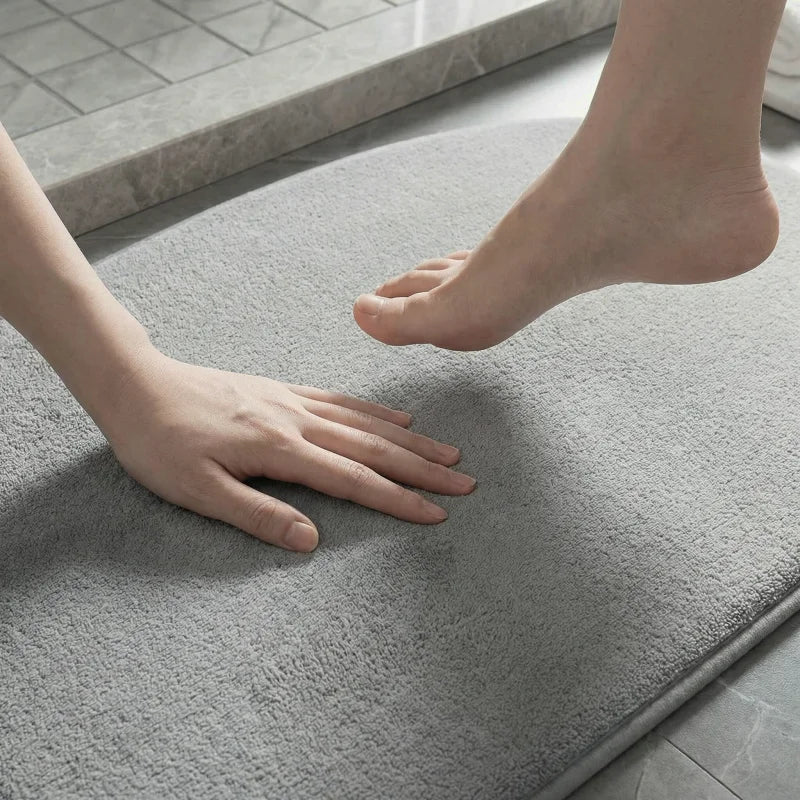 Main touchant le tapis de bain gris à mémoire de forme gris.
